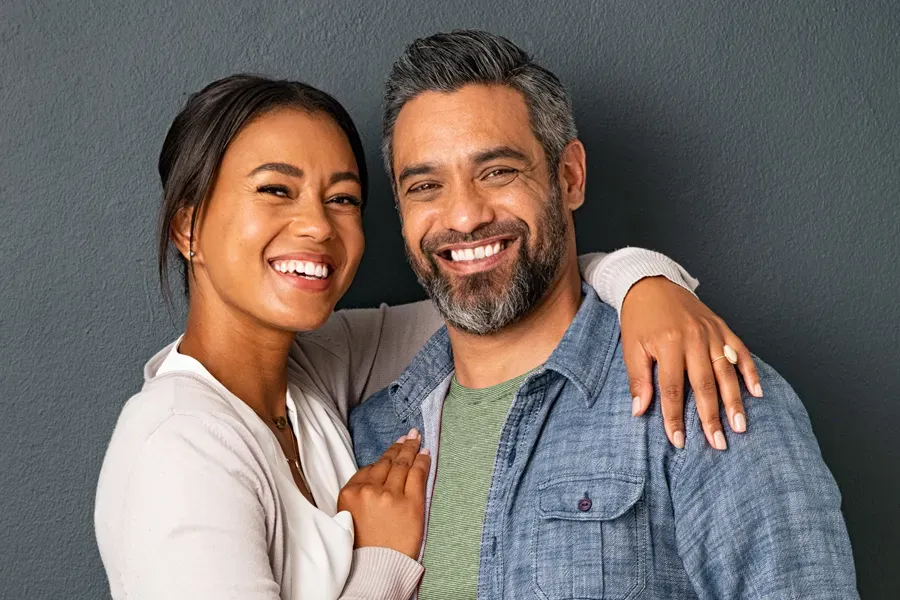 Bioidentical-Hormone-Therapy-Doctor A middle-aged couple with their arms around each other standing against a gray background and smiling, happy with the bioidentical hormone therapy they received from Healthy Aging Medical Centers of New Jersey in Northern New Jersey.