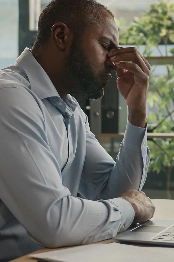 Chronic-Fatigue-Treatment A black man rubbing the top of his nose at his desk, in need of chronic fatigue treatment from Healthy Aging Medical Centers of New Jersey in Northern New Jersey.