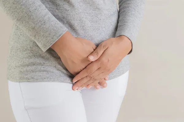 Fibroids-Clinic Close up of a woman in a gray shirt and white pants holding her hands below her abdomen in discomfort. Get treatment for fibroids from Healthy Aging Medical Centers of New Jersey in Northern New Jersey.