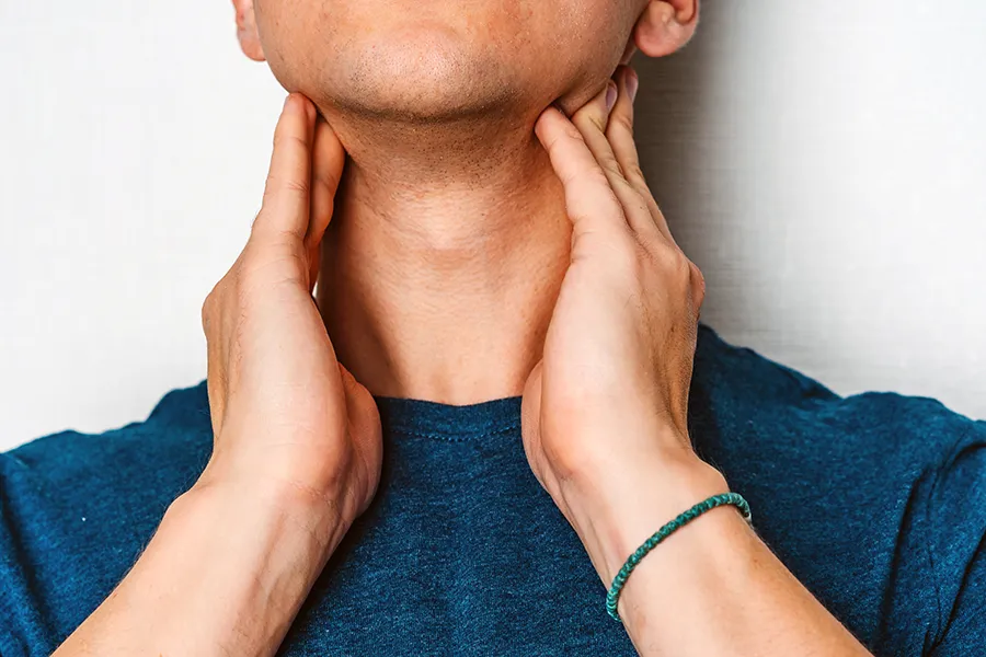 Hypothyroidism-Clinic A man in a dark teal shirt rubs the lymph nodes on his neck. Get hypothyroidism treatment from Healthy Aging Medical Centers of New Jersey in Northern New Jersey.