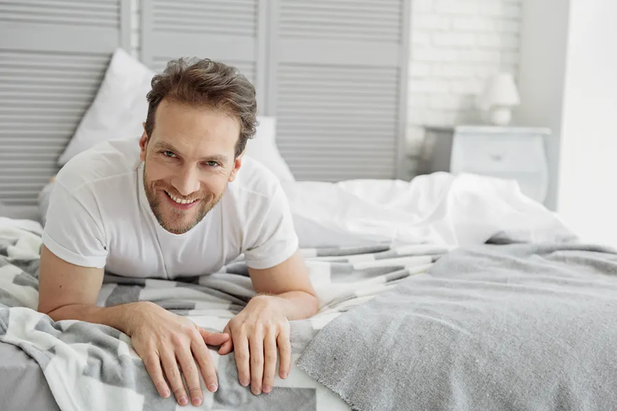 Low-Libido-in-Men-Doctor A dirty-blonde haired man lays on his stomach in bed smiling. Schedule treatment for low libido in men from Healthy Aging Medical Centers of New Jersey in Northern New Jersey.