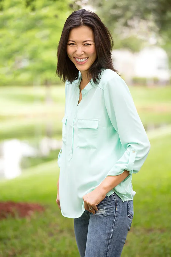 Perimenopause-Treatment A middle-aged brunette woman in a light green button-up shirt stands outside smiling, happy with her perimenopause treatment from Healthy Aging Medical Centers of New Jersey in Northern New Jersey.