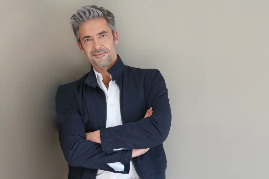 Testosterone-Low-T-Solutionsn-Clinic A middle-aged man in a white shirt and dark blue jacket leans against a gray wall smiling. Get testosterone for Low T from Healthy Aging Medical Centers of New Jersey in Northern New Jersey.